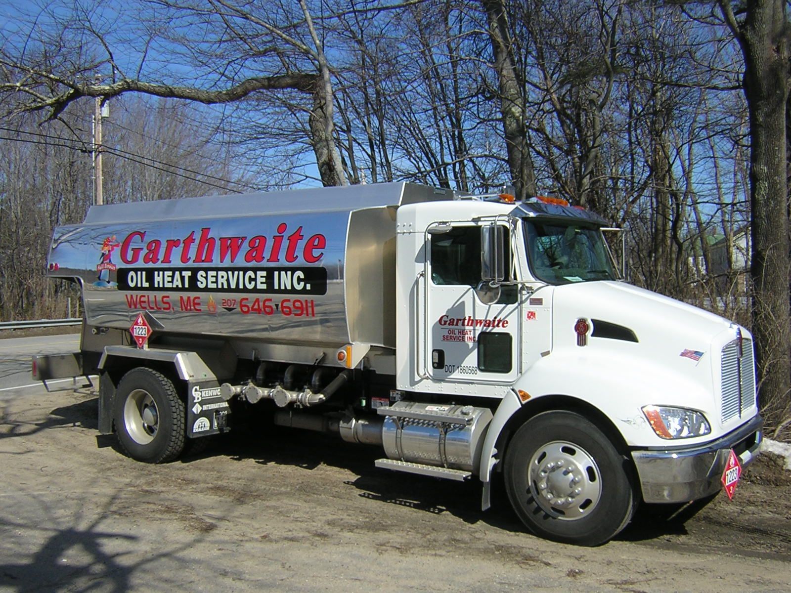 White tanker truck on a grassy roadside against a blue sky with clouds.