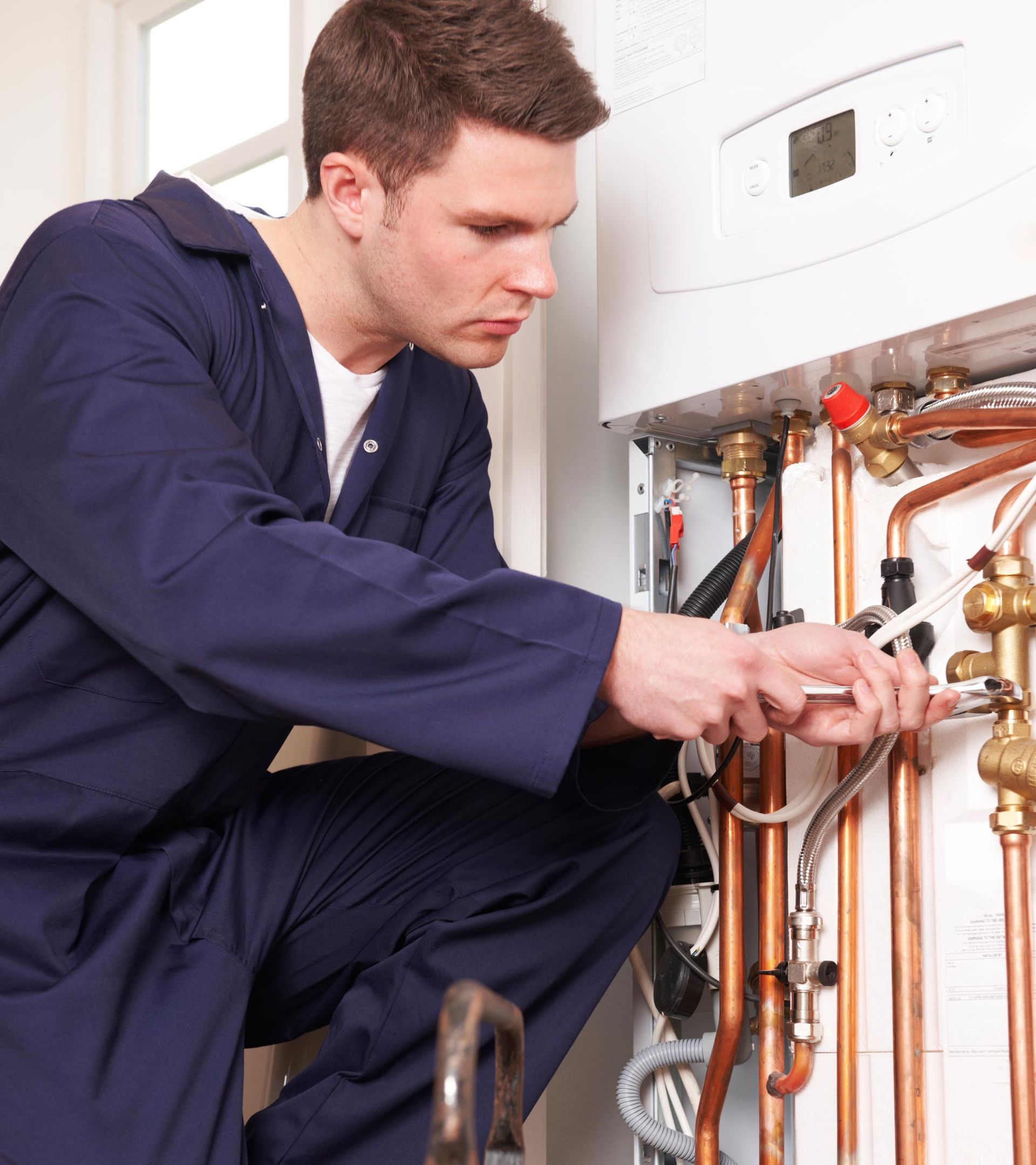 Man in blue jumpsuit, working on a boiler, using a wrench.