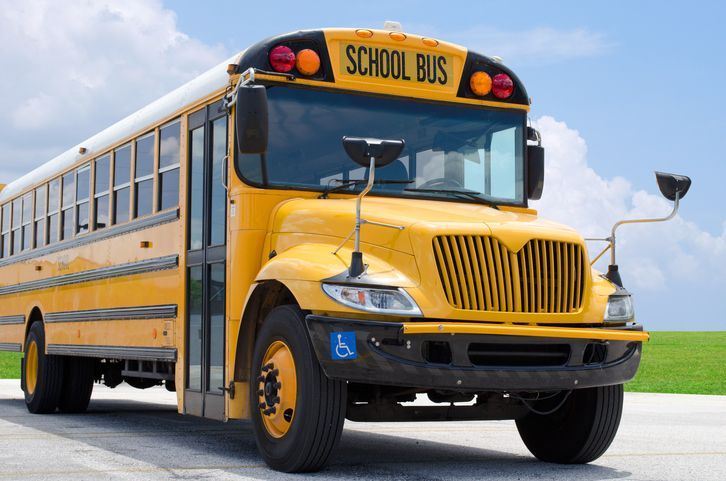 Yellow school bus parked on a road, blue sky background.