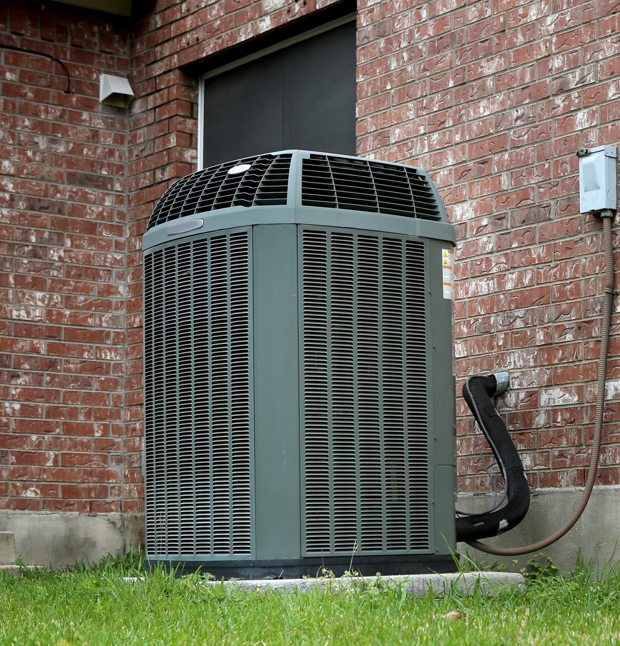 Gray air conditioning unit outside a brick building.