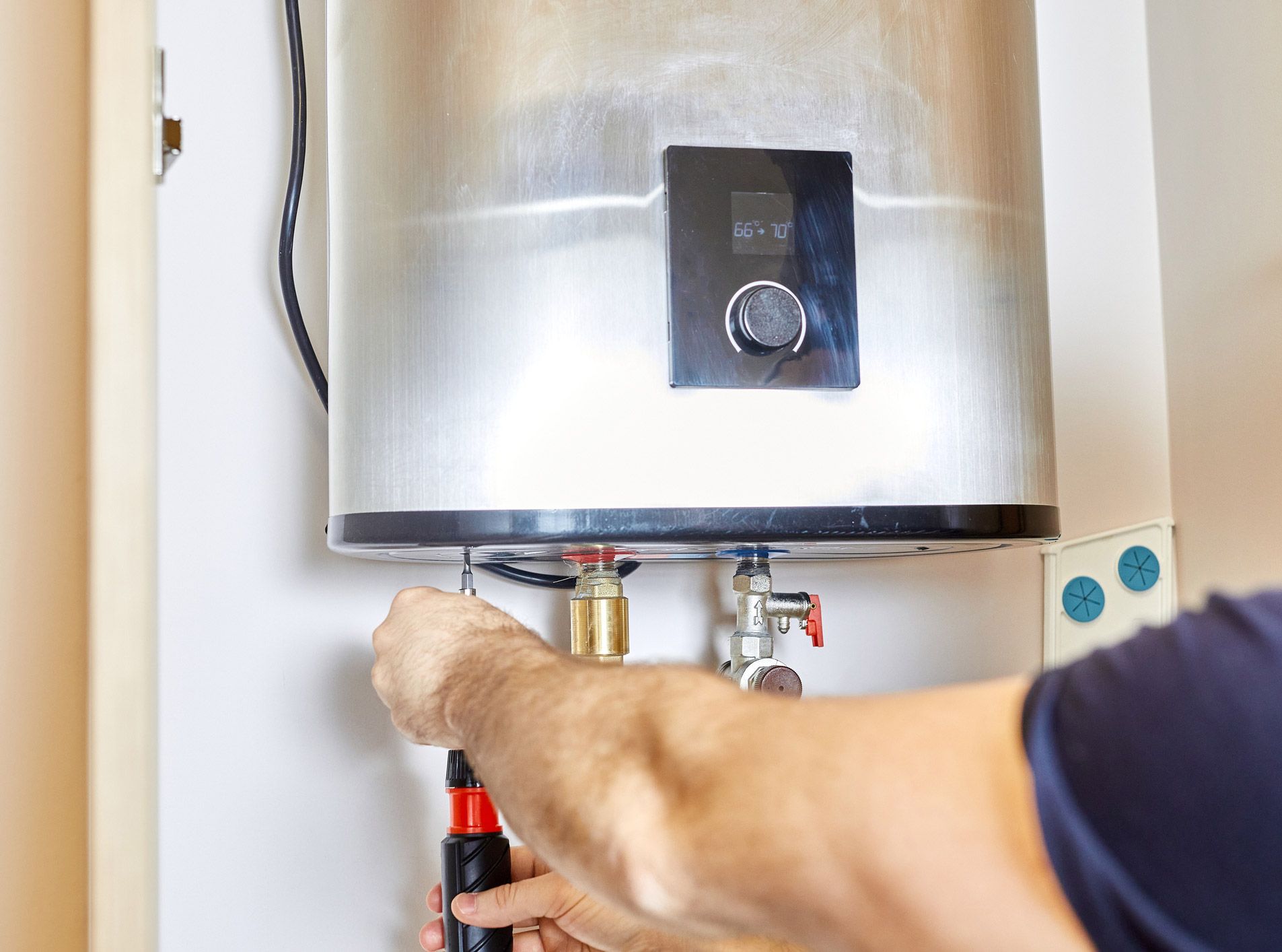 Person using a screwdriver to work on a water heater in a utility closet.
