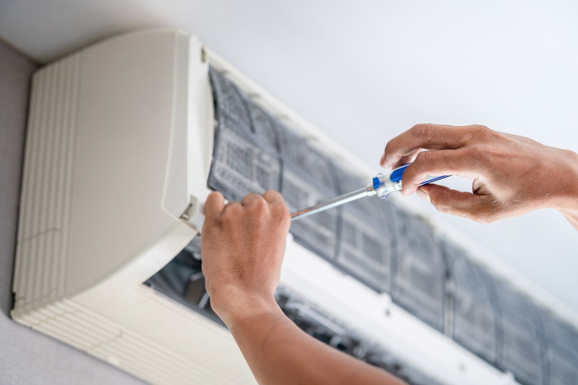 Person using a screwdriver to open an air conditioning unit for maintenance.
