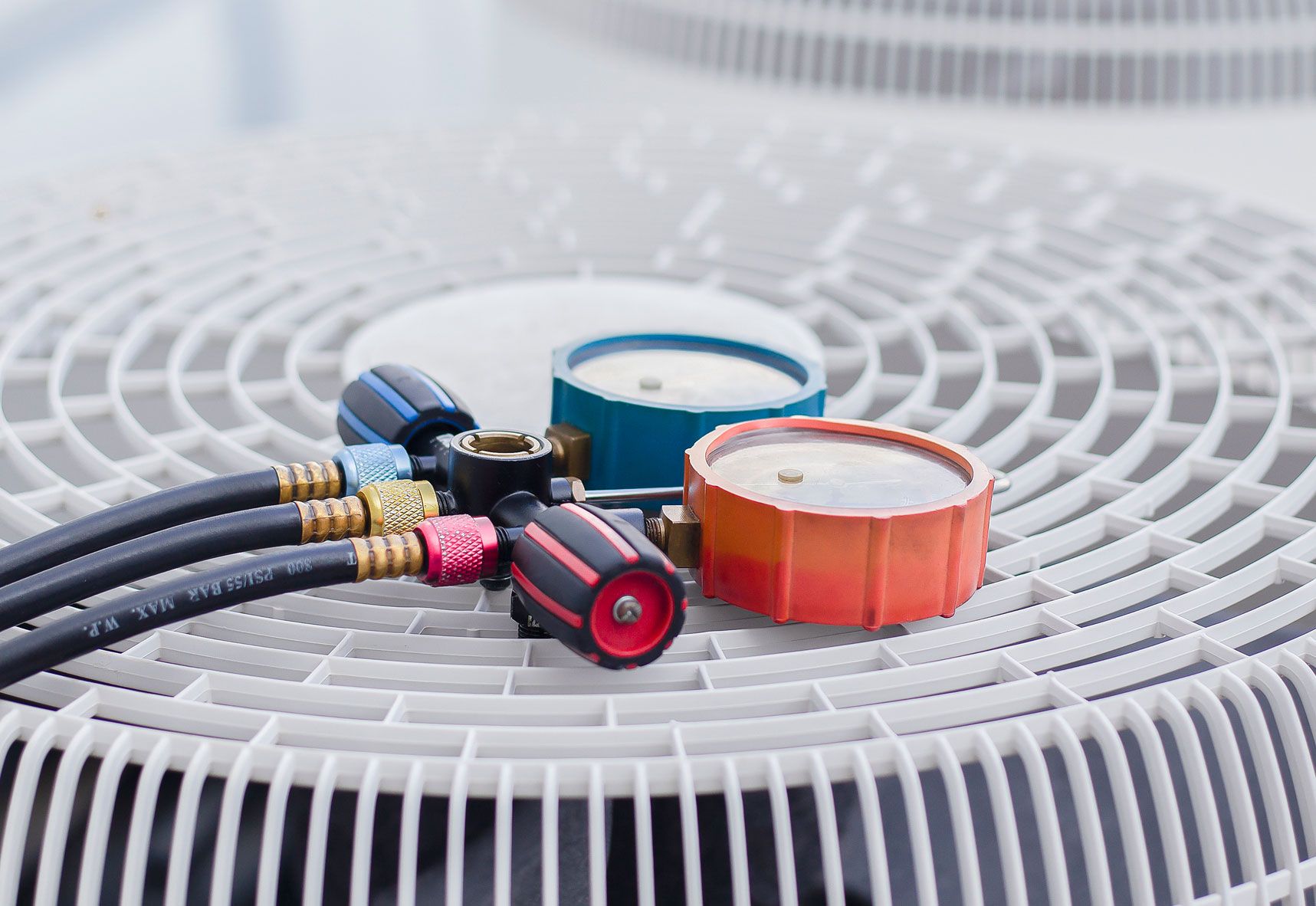 HVAC gauges with colored hoses on an outdoor air conditioning unit's fan grille.