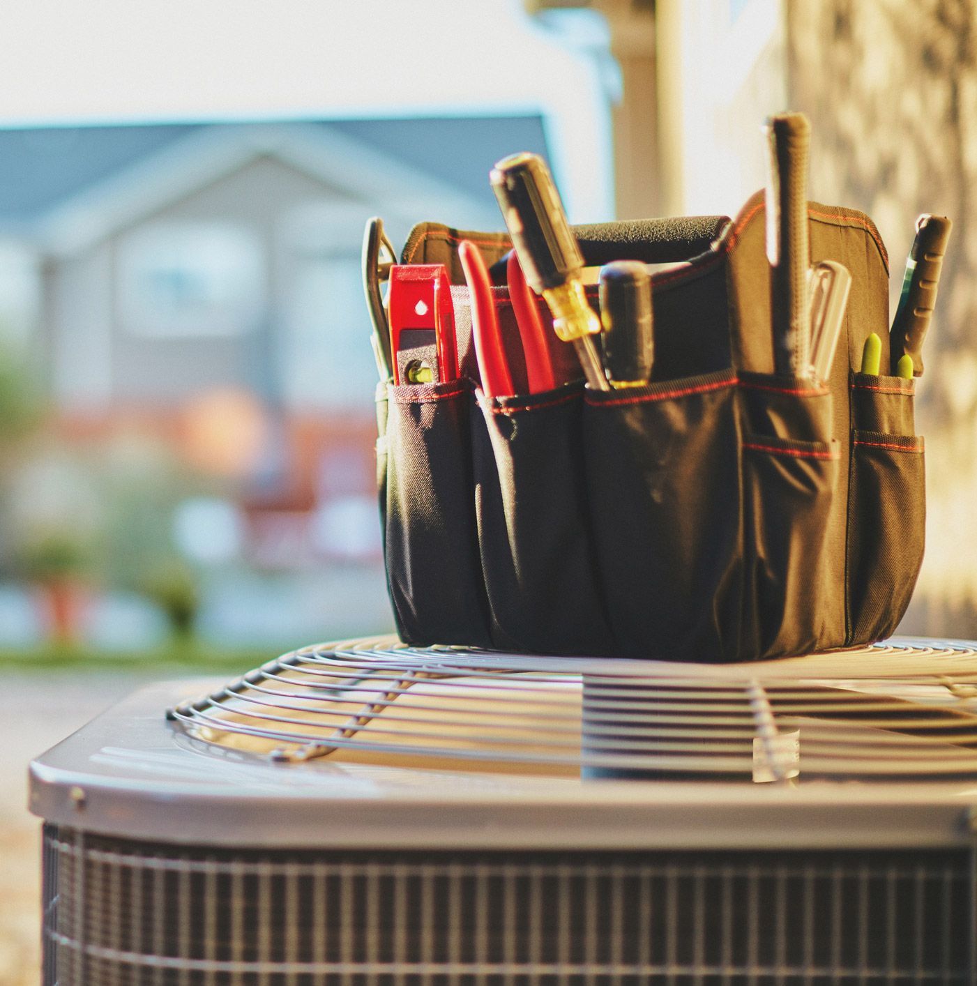 Tool bag with tools on top of an air conditioning unit. A house is visible in the background.