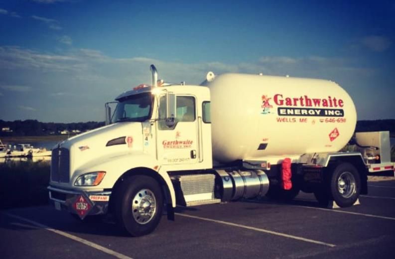 White propane tank with attached valve and regulator, protected by a metal shield.
