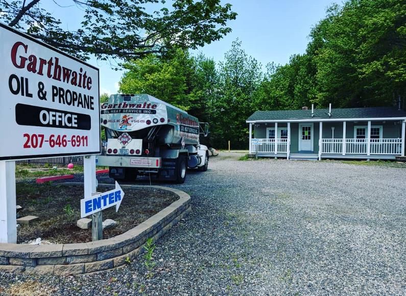 Tanker truck carrying flammable liquids on a road, flanked by trees.