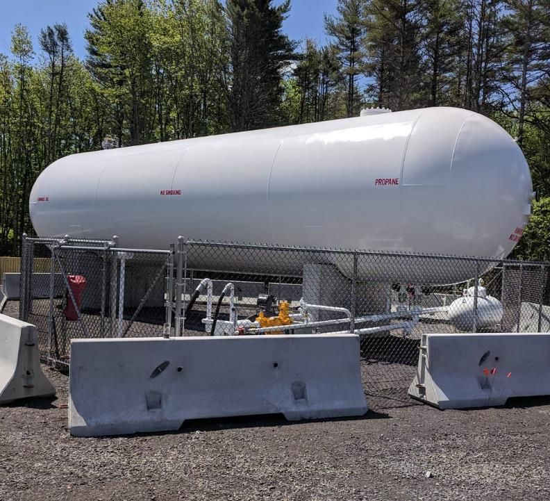 White propane tank with red cap, 'Propane' in red lettering, sits on legs in a snowy yard.