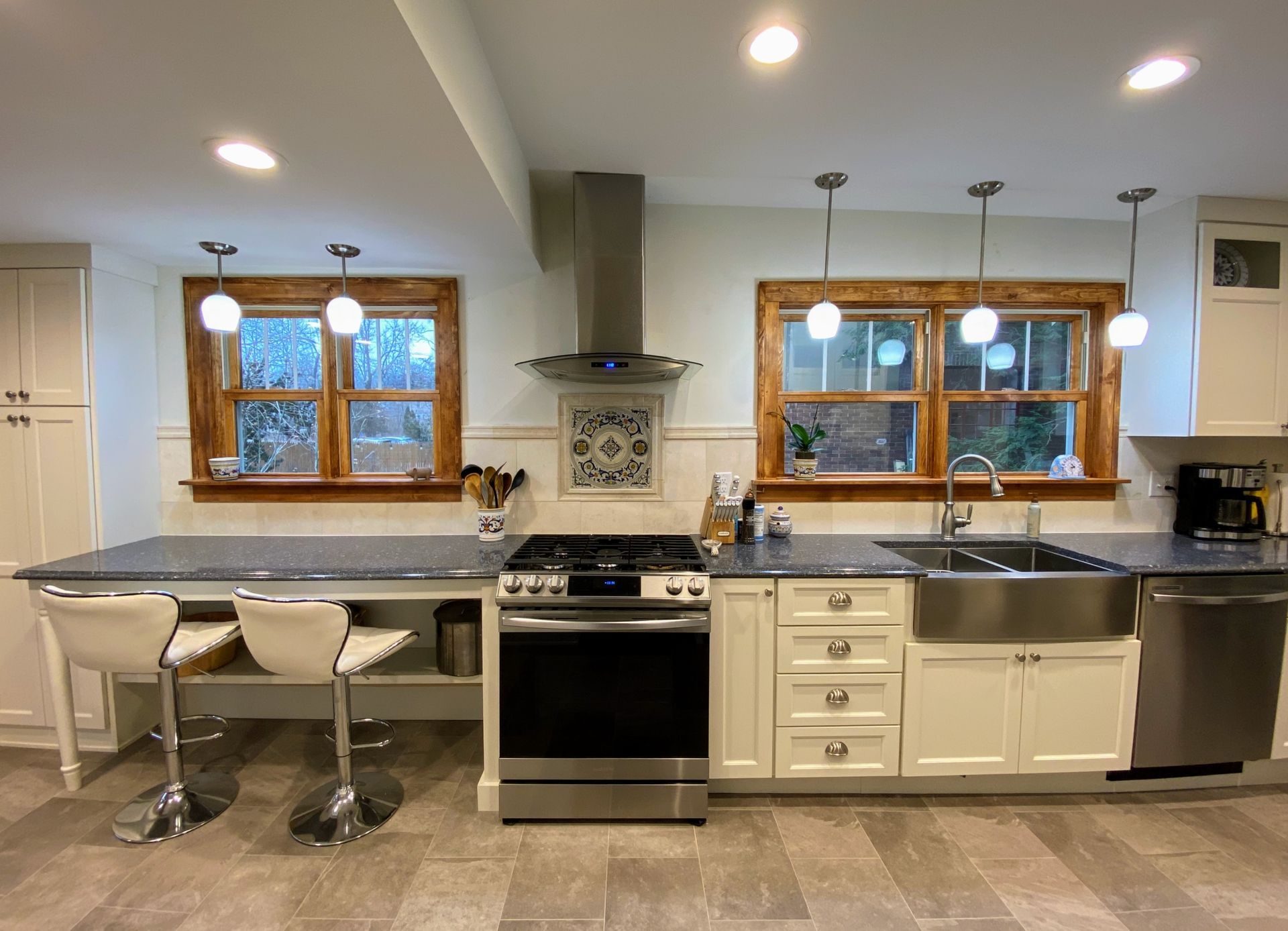 A kitchen with white cabinets , stainless steel appliances , a stove , sink , and two windows.