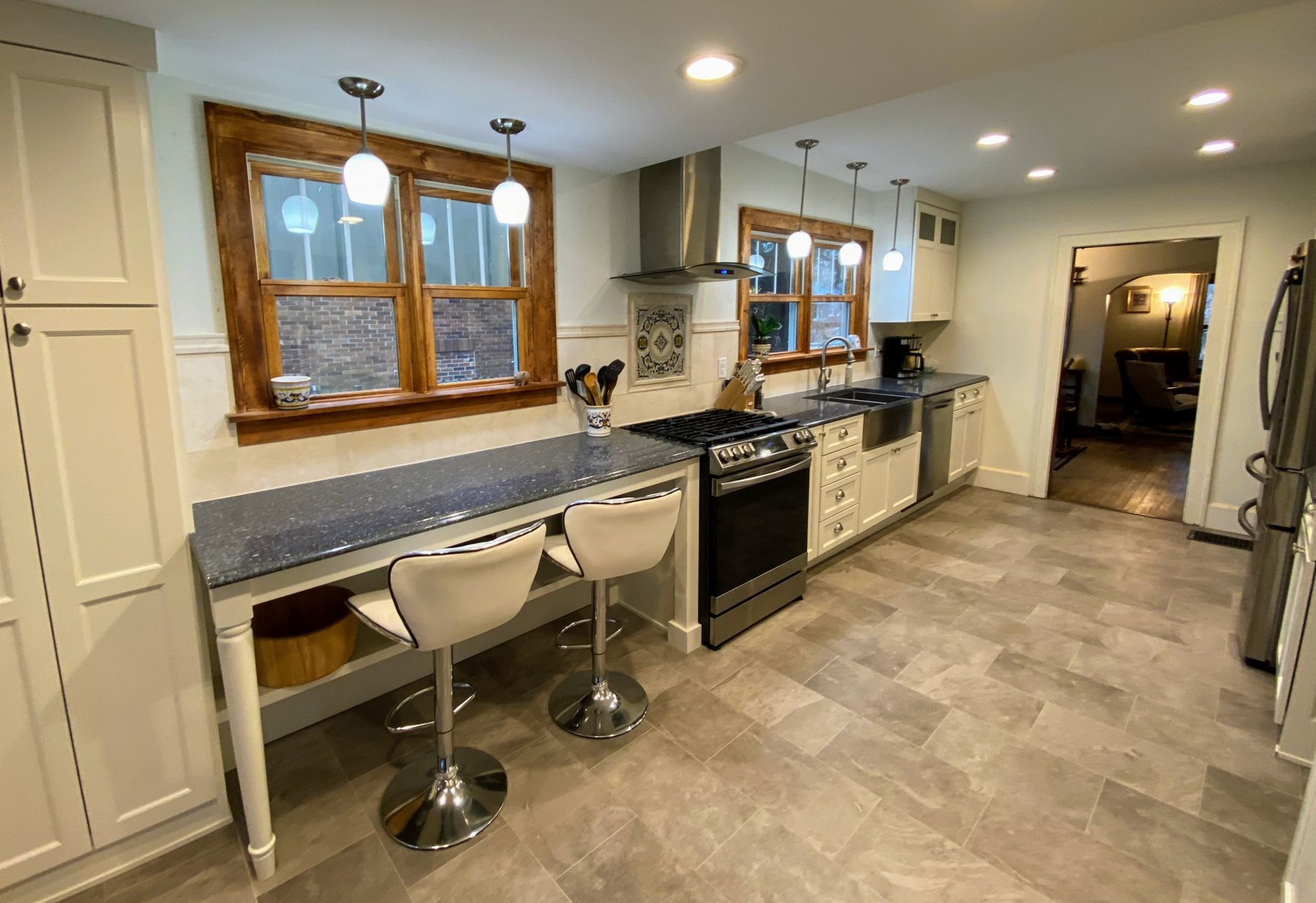 A kitchen with stools , a stove , a refrigerator , and a window.