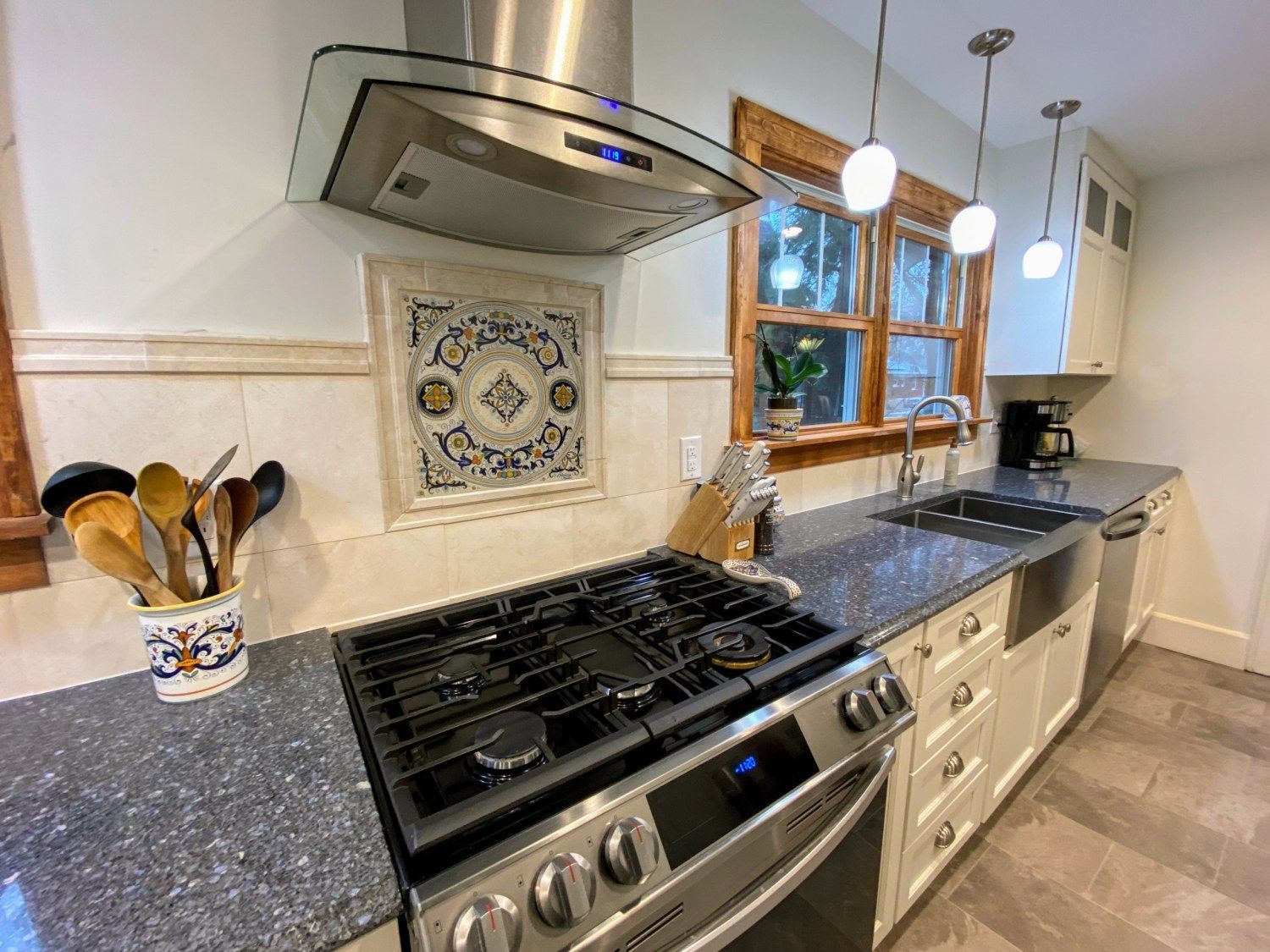 A kitchen with a stove , oven , sink and utensils on the counter.