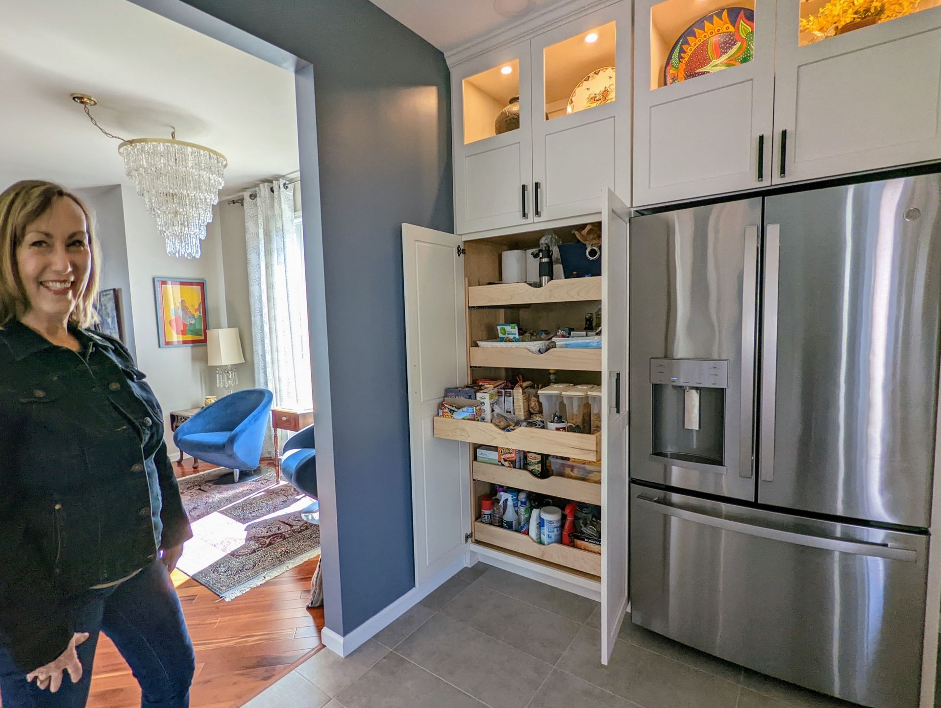 A woman is standing in a kitchen next to a stainless steel refrigerator.