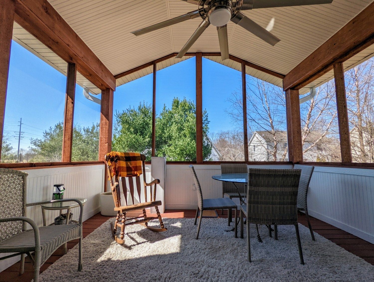 A screened in porch with a rocking chair , table and chairs.