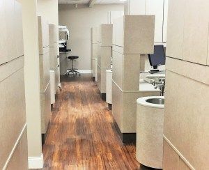 A hallway in a dental office with wooden floors and white cabinets.