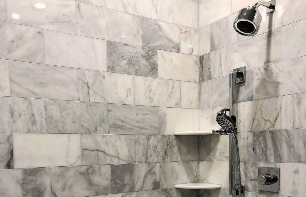 A bathroom with marble tiles and a shower head.