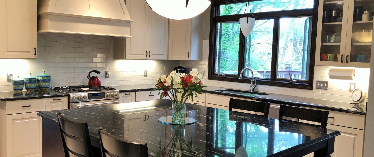 A kitchen with white cabinets , black counter tops , and a large island.