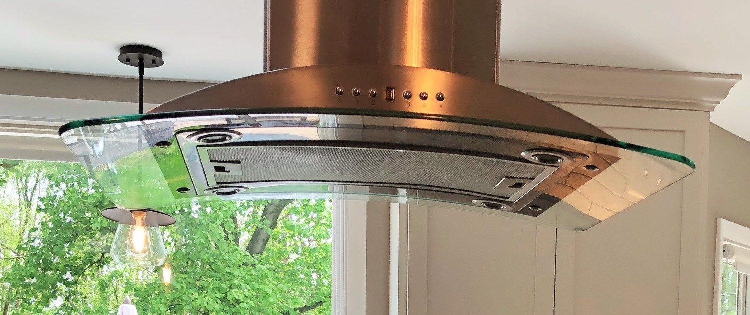 A stainless steel hood with a glass top is hanging from the ceiling in a kitchen.