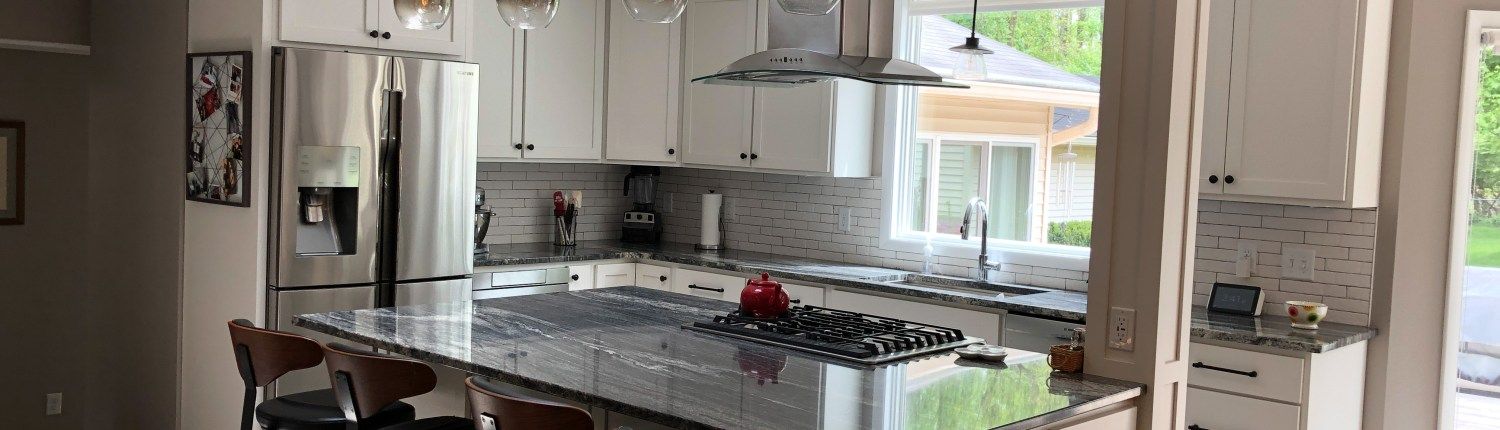 A kitchen with white cabinets , granite counter tops , stainless steel appliances and a large island.