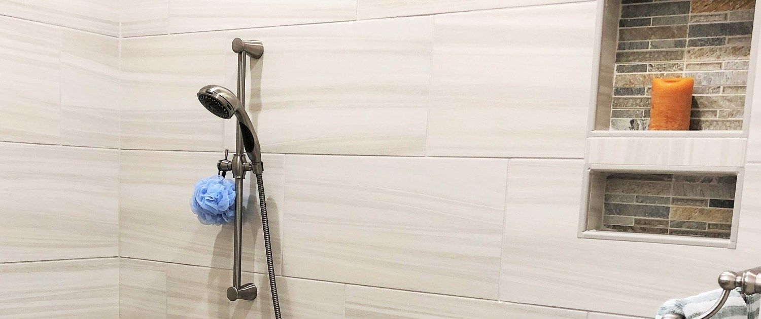 A shower with a sponge and a candle on the wall.