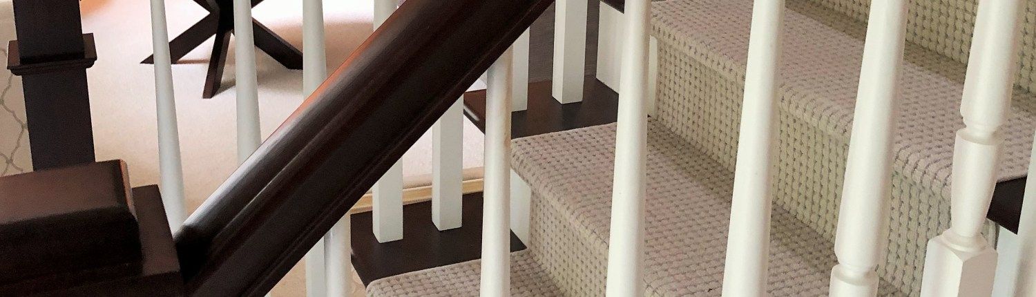 A close up of a staircase with a wooden railing and a carpeted staircase.