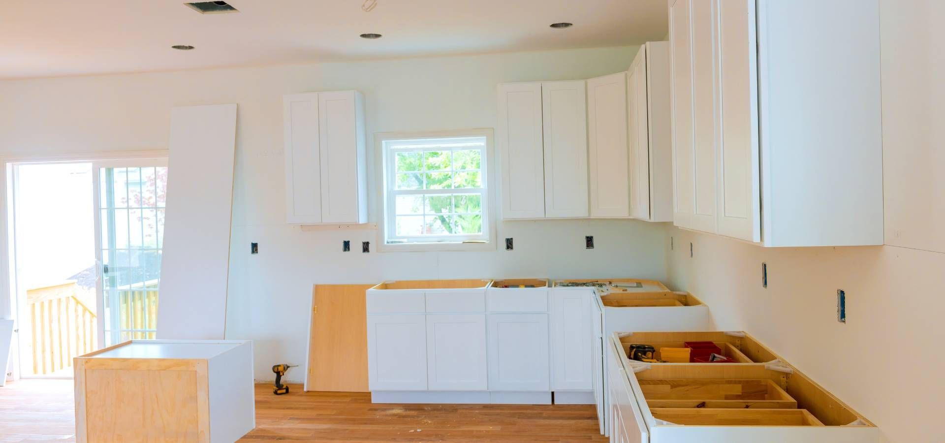 A kitchen under construction with white cabinets and wooden floors.