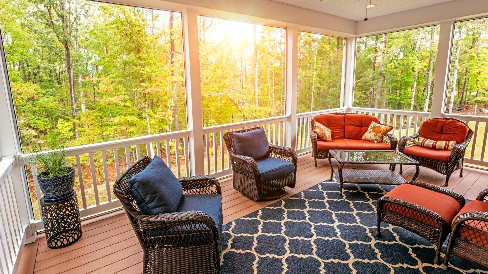 A screened in porch with wicker furniture and a rug.