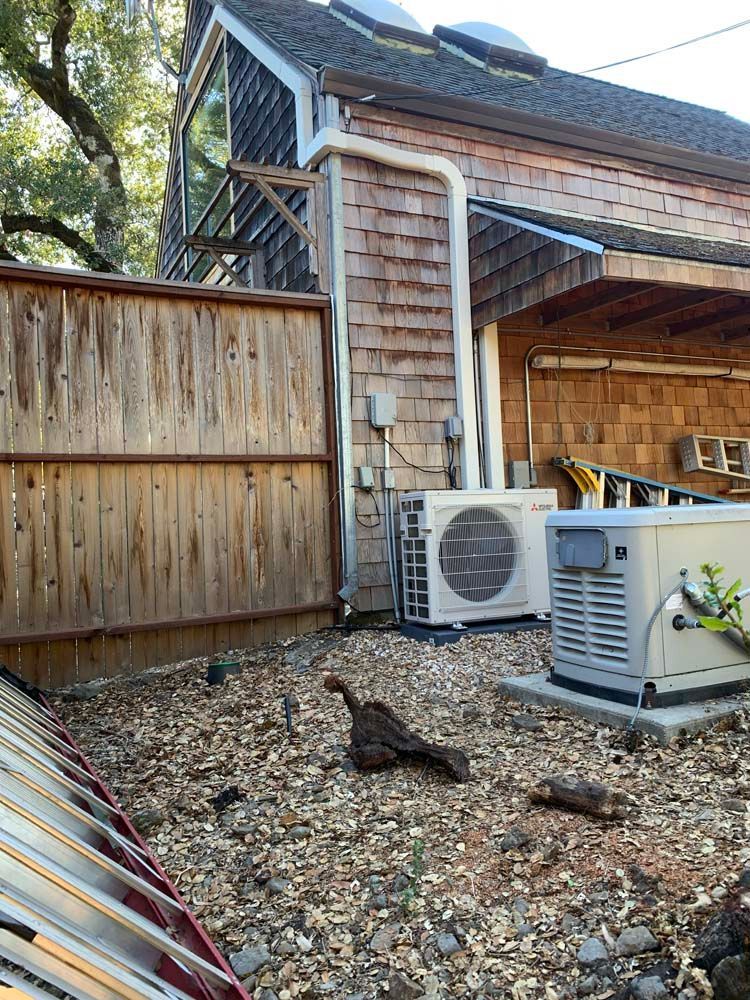 Mitsubishi heat pump unit mounted on a concrete pad next to a building wall with electrical conduit.
