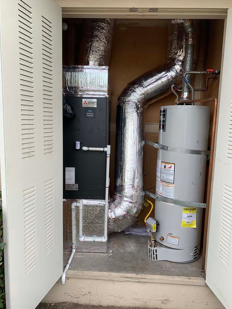 An outdoor utility closet with an HVAC unit and a water heater, both silver and gray, with an open door.