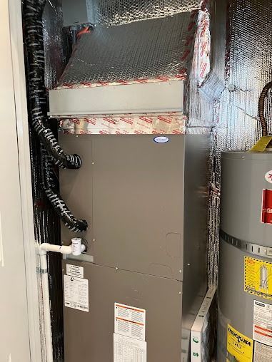 HVAC unit in an enclosed space next to a hot water heater. Ductwork and insulation visible.