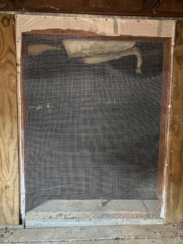 Rectangular opening in a wooden wall, covered with a black and white mesh. Insulation is visible behind the mesh.