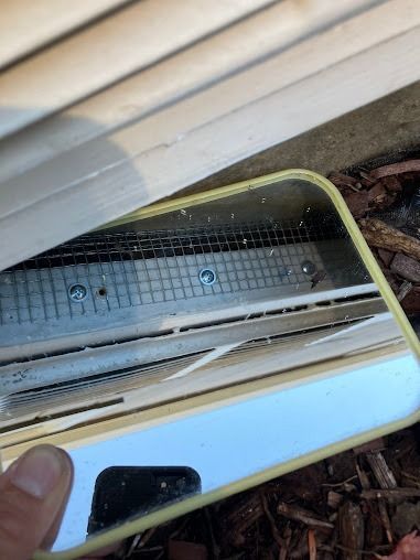 Close-up of a vent with a metal grate and screws, seen through a reflecting phone screen.