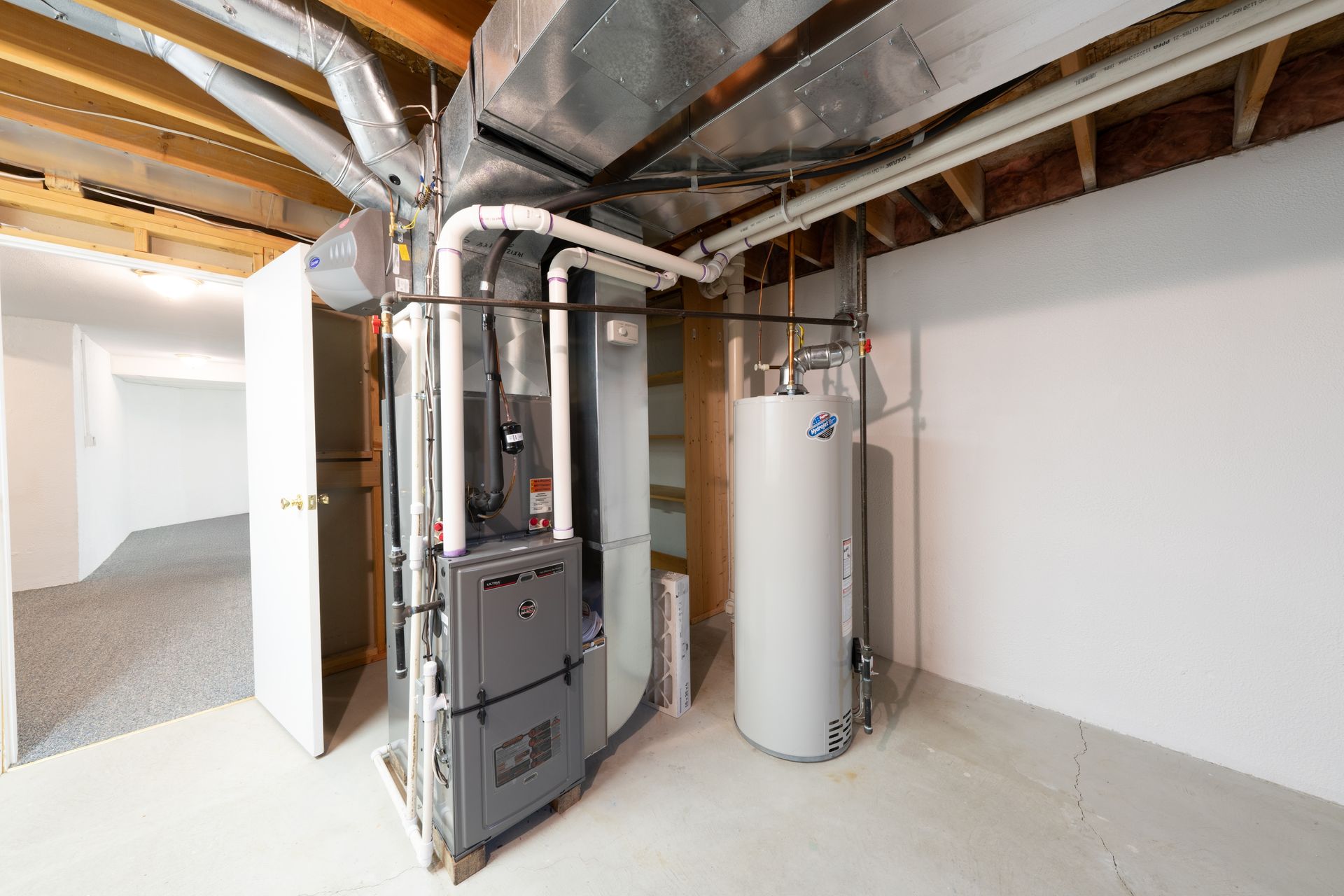 Basement with furnace, water heater, ductwork, and partially visible room with open door.