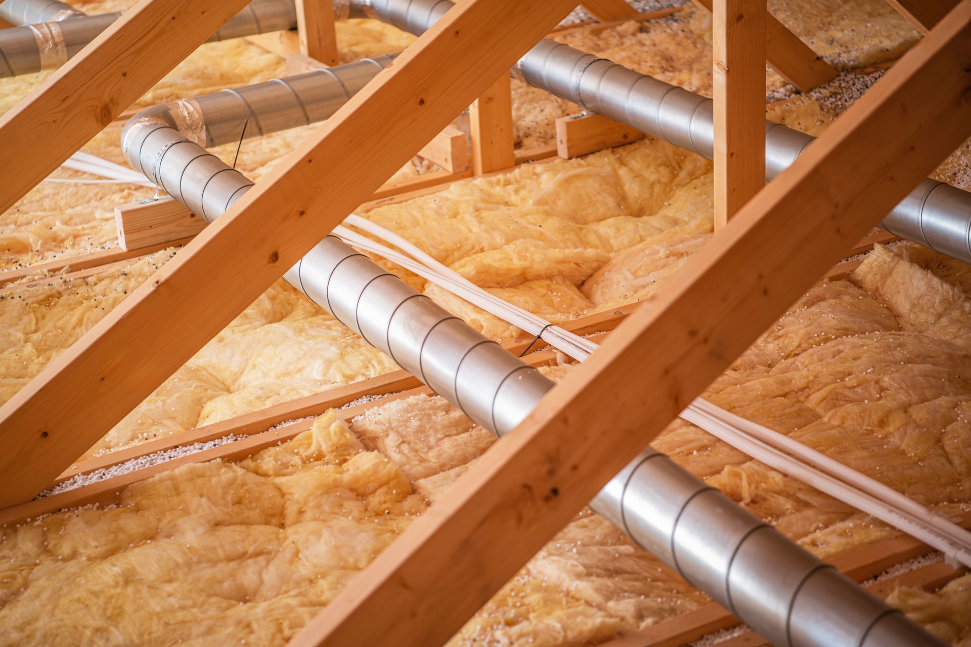 Wooden rafters, insulation, and ductwork in an attic space.
