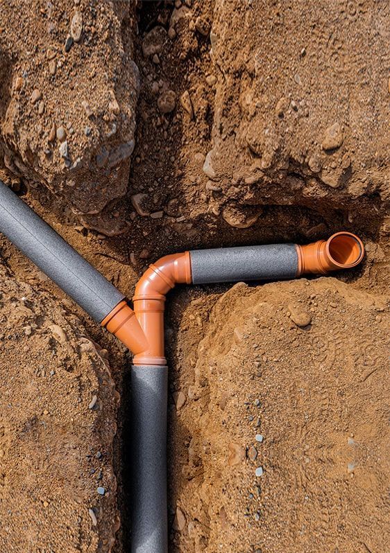 Orange and gray PVC pipes joined in a dirt trench underground