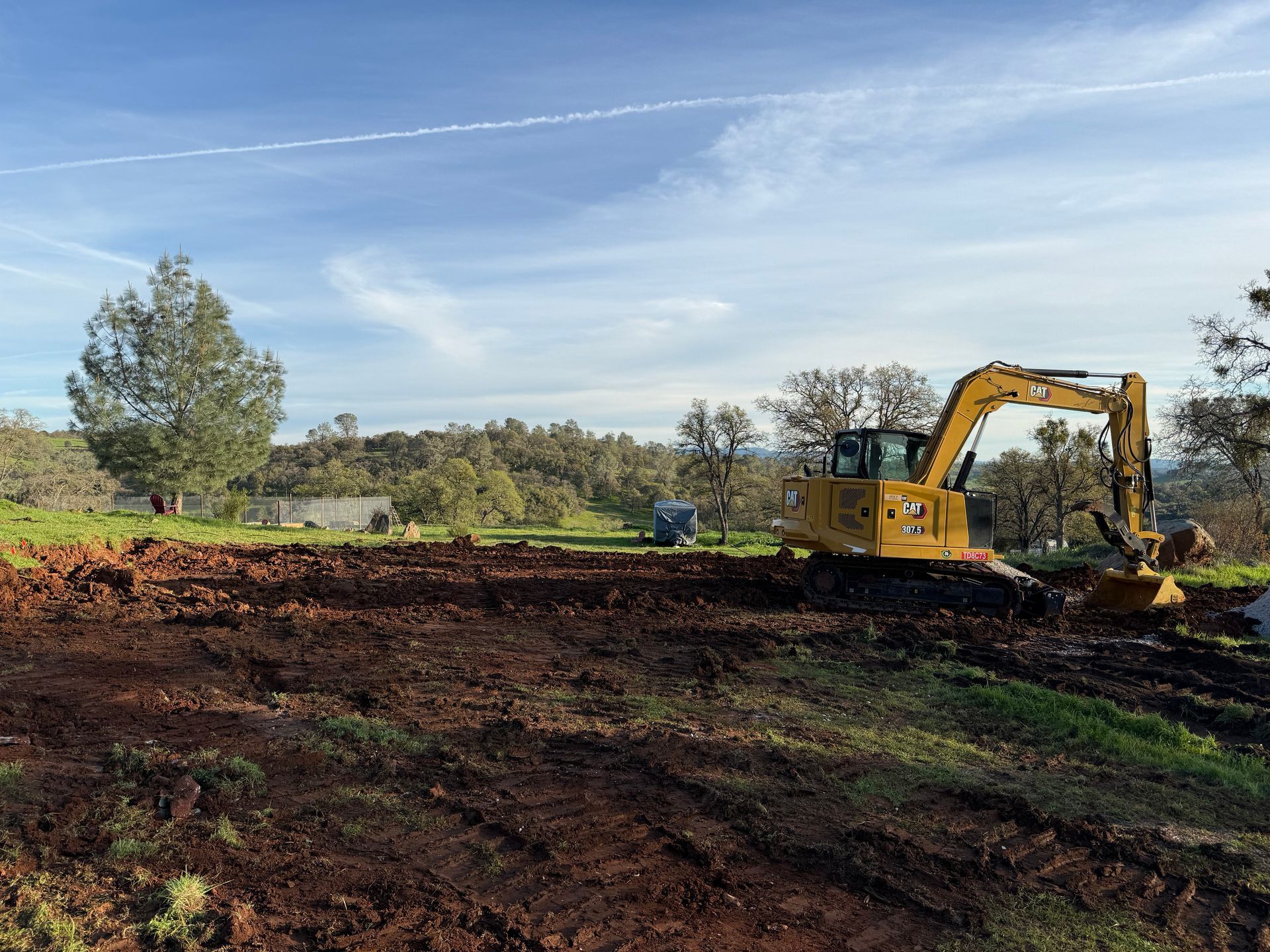 Yellow excavator clearing a dirt field under a blue sky with trees in the background