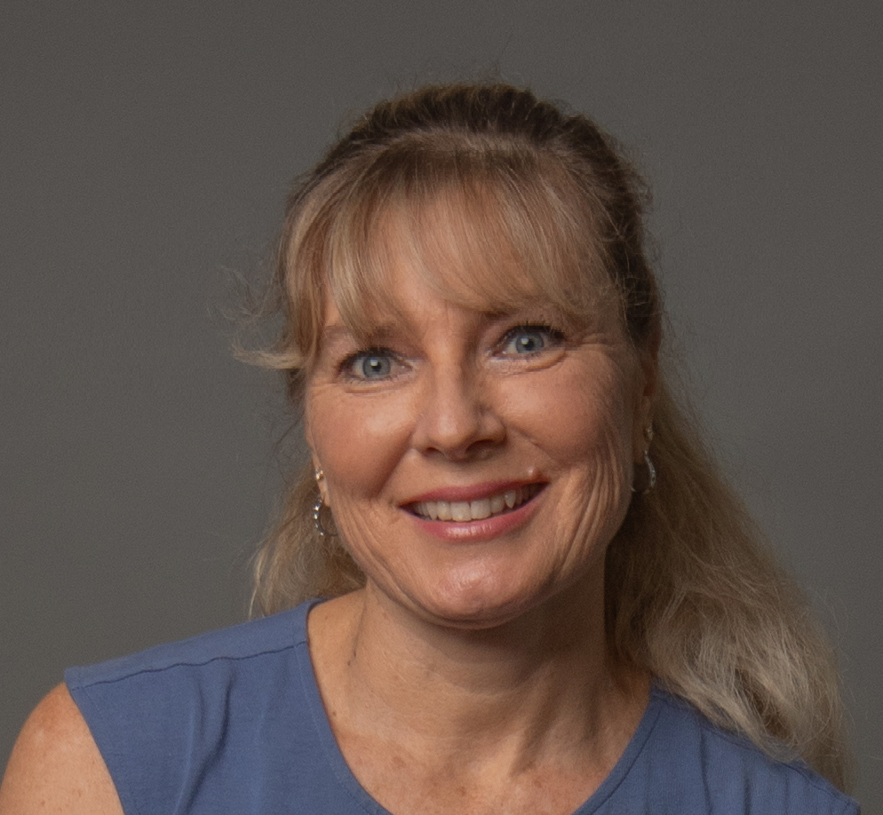 Smiling woman with blonde hair, wearing a blue shirt, against a gray backdrop.