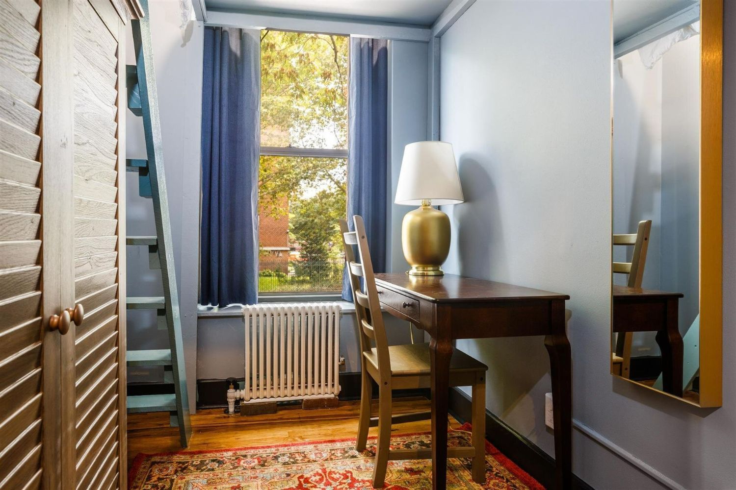 a small room with a desk , chair , lamp and mirror .