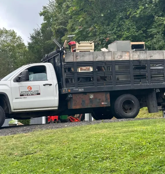 A white pickup truck with a flatbed full of scrap metal parked on a grassy hill. The truck has a business logo on the door.