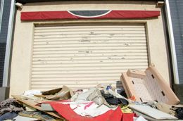 Closed storefront with a metal roll-up door; a pile of trash and debris is in front.