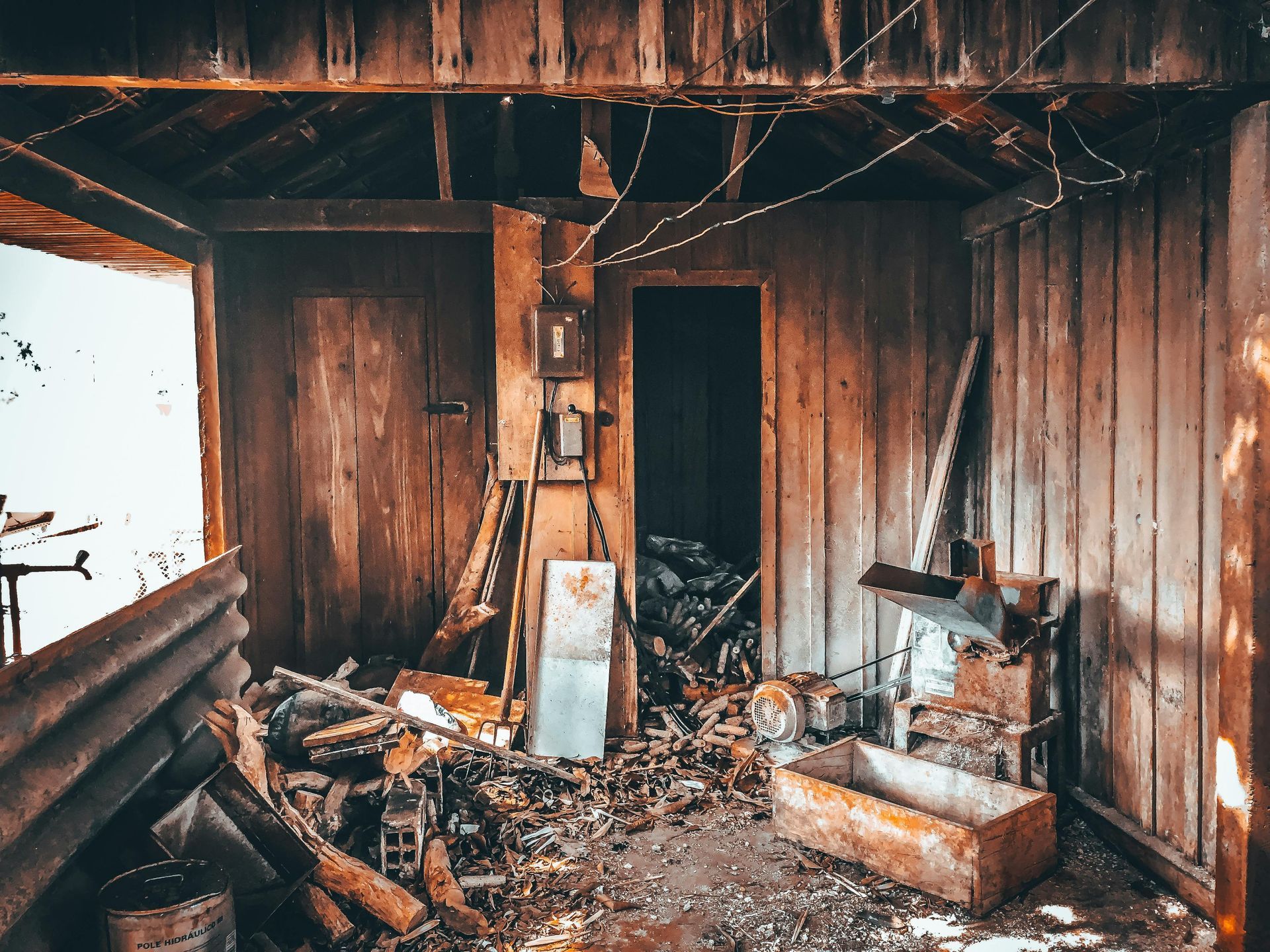 Interior of a dilapidated wooden building. Debris litters the floor; a doorway leads to darkness.