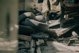 Pile of tires and wooden planks with a person in boots standing nearby, likely in a dilapidated outdoor setting.