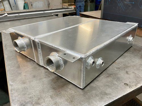 Metal rectangular tank with welded fittings on a workbench.