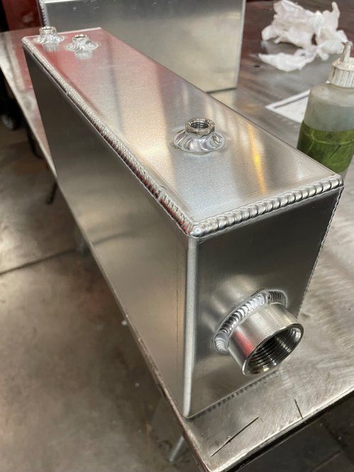 Silver metal rectangular tank with welded seams, fittings, on a metal table.