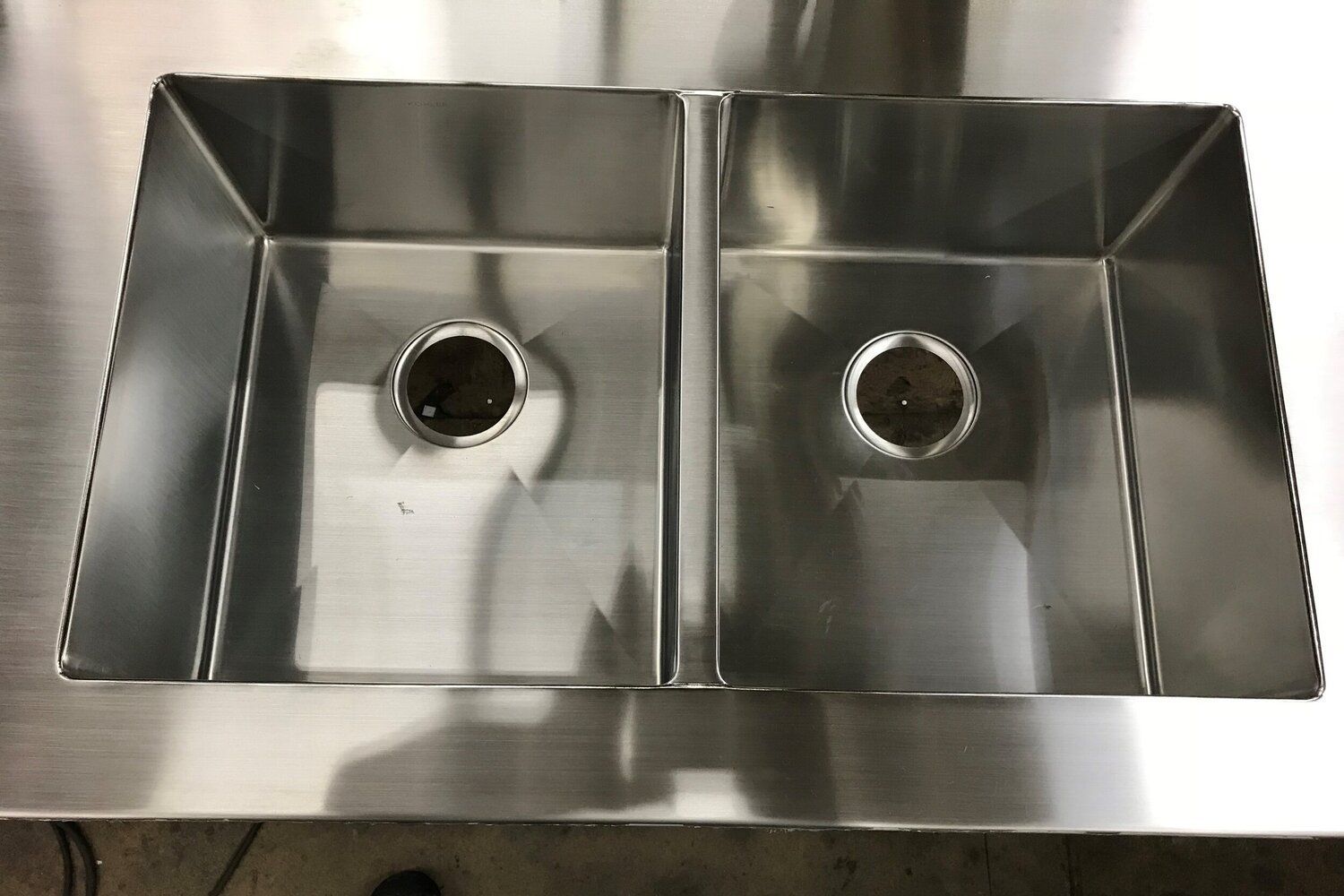 Two stainless steel kitchen sinks side-by-side with drain holes, set in a stainless steel countertop.
