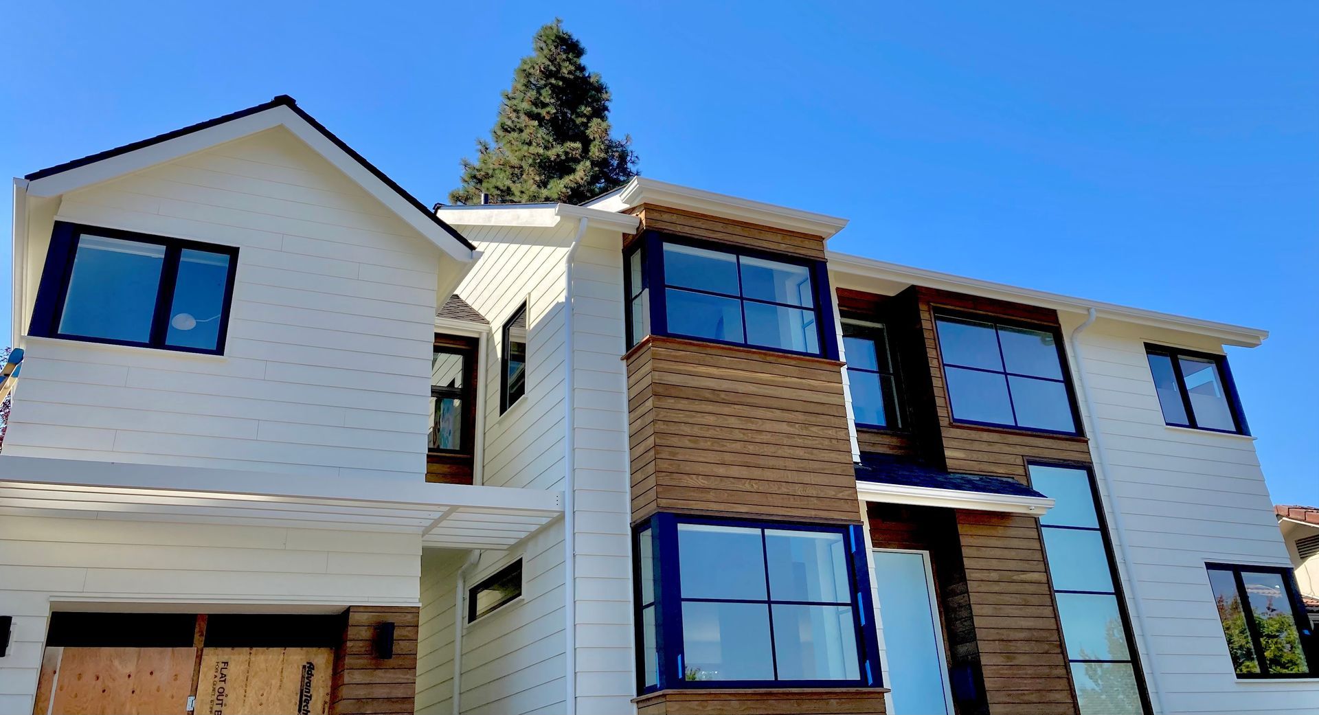 Two-story house with white siding, brown brick accents, large windows, and a blue sky background.