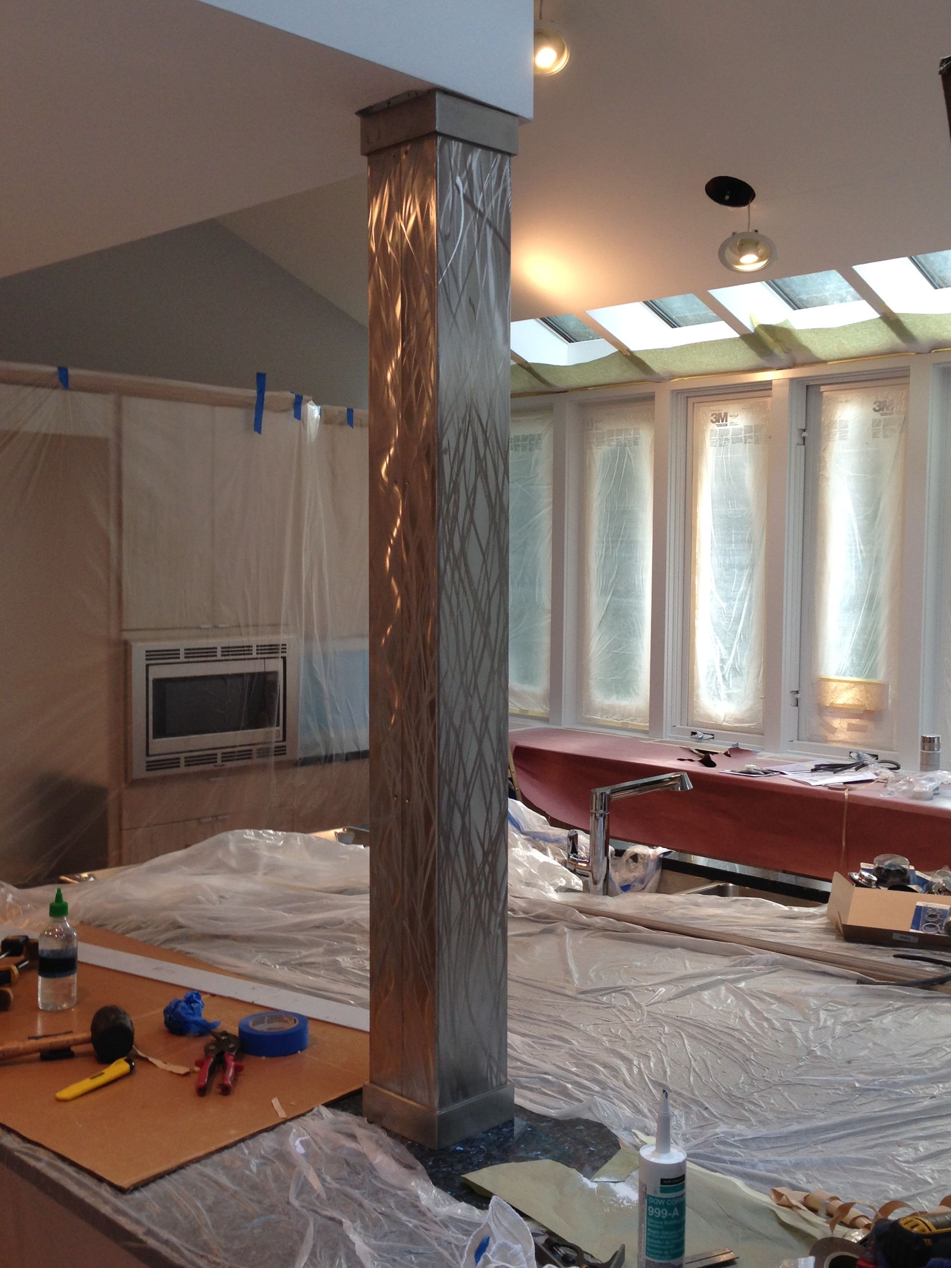 Tall decorative column with textured surface in a room under construction, with covered surfaces and tools.