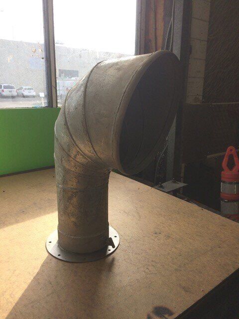 Metal, bent ventilation pipe on a table, with a round base and an angled opening.