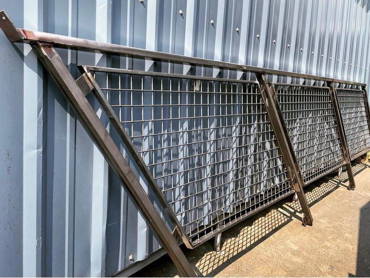 Metal fencing panels with grid and diagonal supports, leaning against a corrugated metal wall.