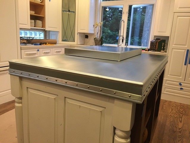 White kitchen island with a metal countertop, cabinets in the background, window.