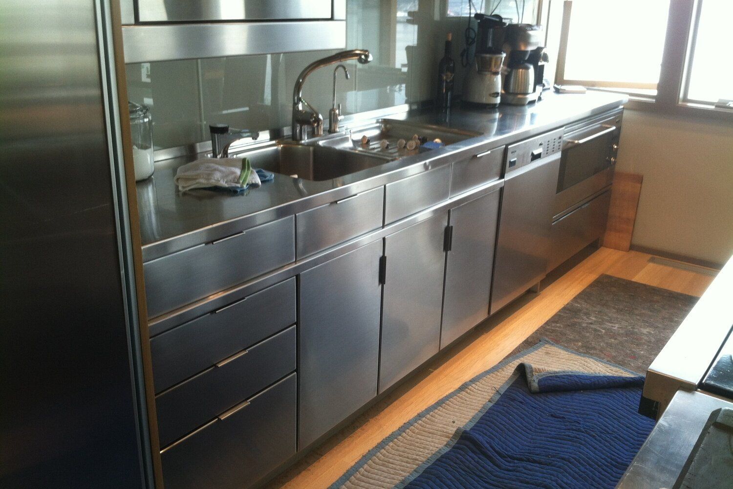 Stainless steel kitchen cabinets and countertop with a sink, appliances, and a window.