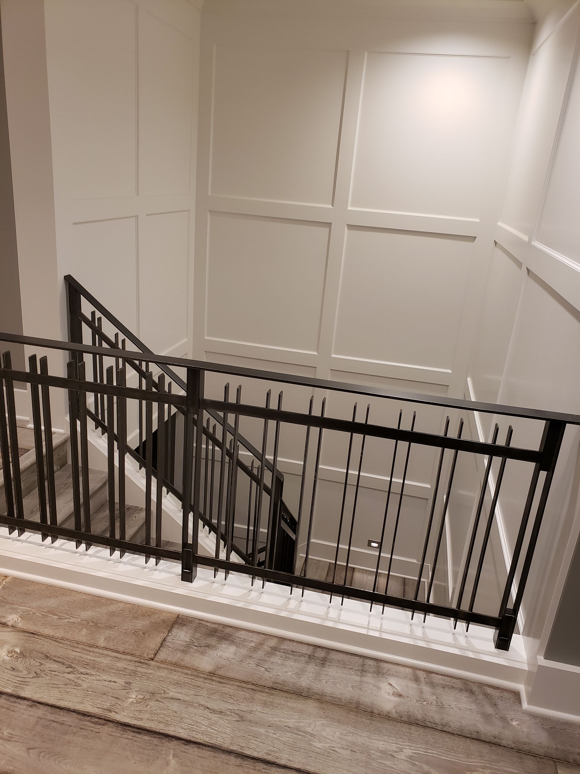 Staircase with black railing and white paneled walls. Downward angle, looking into the stairwell.